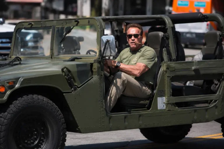 Arnold Schwarzenegger driving his signature olive drab Hummer H1 with doors removed on Los Angeles streets representing the most recognizable image from his car collection of approximately 20 to 25 vehicles worth an estimated 4 to 5 million dollars spanning military vehicles luxury European cars electric vehicles and classic American automobiles with the Hummer H1 being the vehicle he was directly responsible for bringing to civilian production by lobbying AM General for years after encountering a military convoy during filming of Kindergarten Cop in 1989
