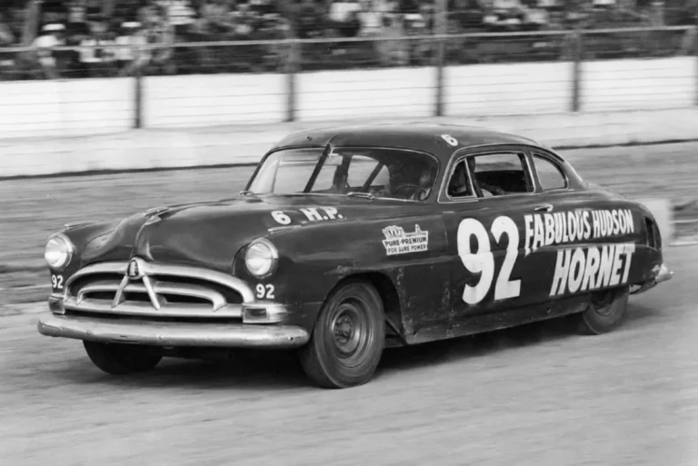 Hudson Hornet competing in NASCAR Grand National racing in 1952 or 1953 showing the step-down unibody construction that lowered the center of gravity below the frame rails giving it an inherent handling advantage that produced 27 victories in 34 races in the 1952 season and more than 80 total NASCAR wins across its competitive life with driver Marshall Teague and Herb Thomas using the 210 horsepower straight six cylinder engine that eventually proved insufficient against the emerging V8 competition