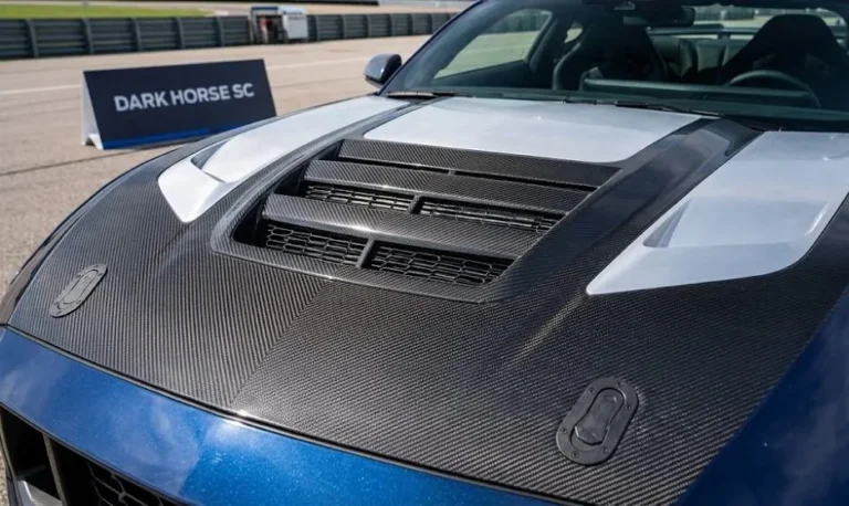 2026 Ford Mustang Dark Horse SC showing the carbon fiber aluminum hood with large cooling vent and standard hood pins that produces 2.5 times more downforce than the standard Dark Horse hood alongside the revised front fascia developed from motorsports experience for improved brake and engine cooling on the new supercharged Mustang